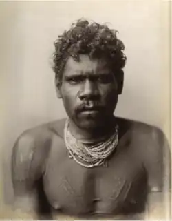 Portrait photograph of a shirtless Aboriginal man wearing a collection of beaded necklaces