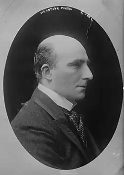 Right profile of white man with bald head except for a small amount of dark hair at the back and sides, clean shaven, with bushy eyebrows