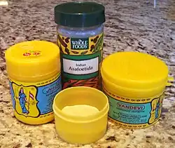 Colour photograph of four plastic containers; in the foreground, the open container holds a yellow powder.