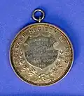 An Auckland Society of Arts medal awarded to A.A. Whitehorne for "Best Part Song" in 1886 by Mrs McCosh Clark. Designed by Anton Teutenberg. Diameter of 45mm. Designs on the front include kowhaiwhai on the outer band, beading, an engraved inner band reading "V.E.C T.A.E. CUM LARIBUS ARTES", and a centre in YM (potentially gold) and lyre. Designs on the back include engraved text reading "AUCKLAND SOCIETY OF ARTS", a shield with engraved text reading "PRESENTED BY / Mrs / McCosh Clark / A.A. WHITEHORNE / FOR BEST / PART SONG / 1886", an "open laurel wreath", and beading. The medal has an attached ring at the top. The designer's name is included on either side of the inner rim with smaller text reading "A.TEUTENBERG / AUCKLAND. N.Z.".