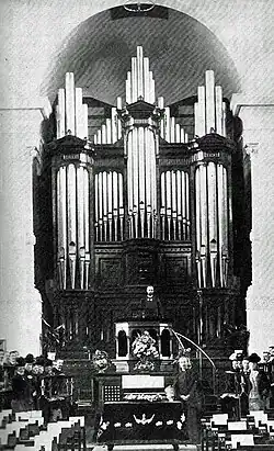 A picture of the interior of a church. A minister is standing in the pulpit in front of a large organ.