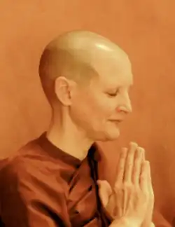 headshot of Tathaloka with her hands at her chest in prayer. Her eyes are closed and her head is shaved.
