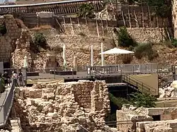 photograph depicting a platform raised over ruins and set against the backdrop of a high stone wall