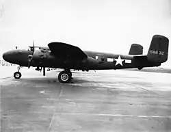Black-and-white photo of an early bomber parked perpendicular to the camera, facing left, rearward of the wing is a star in front of horizontal stripes