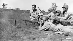 Group of U.S. Army soldiers outdoors in a field during training; an instructor and trainees crouch as a Browning Automatic Rifle is demonstrated.