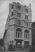 A narrow stone-faced façade with two bays of windows, arched at first floor level and decreasing in size on the floors above