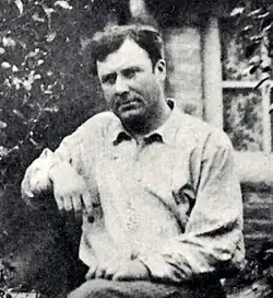 Black-and-white photograph of Atget sitting outdoors, wearing a loose shirt and gazing at the camera