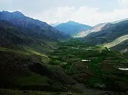 A lush green valley with a web of farm plots along the bottom