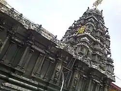 A black granite construction of a temple tower with a metal disc and miniature at the top