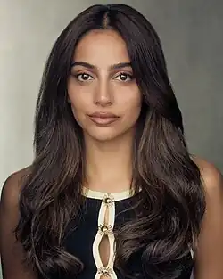 Banita Sandhu wearing a black sleeveless top with white trim, looking directly at camera