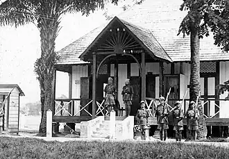 Small building, kinda like a shack. Few guards out front posted up with rifles, bayonettes attached. Stern lookin Indian dudes standing on the porch looking at the camera like they finna come down if you get too close.