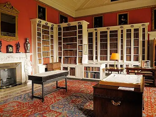 Room has white bookshelves against the walls with oil paintings hung above