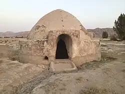 Domed adobe structure with an arched entrance standing in an open, arid landscape.