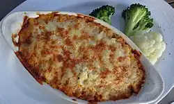 Pie with mashed potato topping, lightly browned on a plate, served with broccoli and cauliflower florets