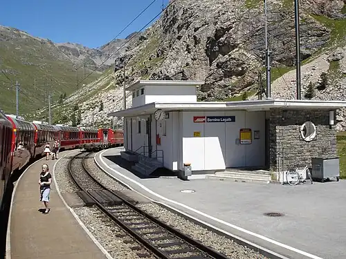 Red train parked at station; the station building is single-story with a flat roof