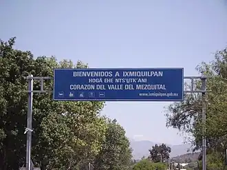 A matte blue sign with trees behind it and a clear blue sky