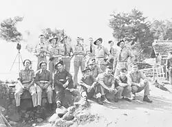 A black and white informal photograph of a group of men in various uniforms; some are seated, some are standing