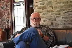 Colour photo of Blaine Larson seated, reading a book at "Little Alps"
