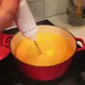 An immersion blender being used to blend soup on the stove