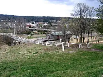Bombala, looking towards the town centre. The footbridge passes over the Bombala railway line. The right most building is the station building, the centre building the goods shed and above that is the bridge over the Bombala River.