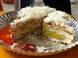 A sandwich with a layer of potatoes, a layer of vegetables, and bread in the middle, topped with cheese