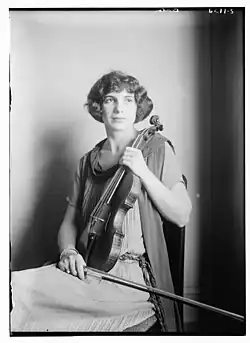 A white woman with bobbed dark wavy hair, seated, holding a violin