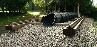 Exterior in woodland. a short section of railway line on wooden sleepers with a cast iron pipe of approximately one foot diameter, running inline with the rails