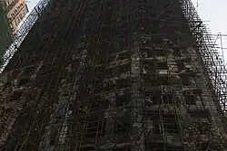 An upward view of a burned-out high-rise: a blackened mess of tangled scaffolding and holes for windows.