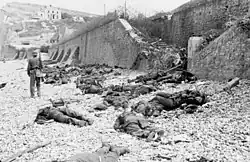 The deadly result of enfilade fire during the Dieppe Raid of 1942: dead Canadian soldiers lie where they fell on "Blue Beach". Trapped between the beach and fortified sea wall, they made easy targets for MG 34 machineguns in a German bunker. The bunker firing slit is visible in the distance, just above the German soldier's head.