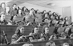 A group of young women, wearing headsets, sitting in an auditorium, controlling projectors.