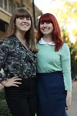 Image 93Two women with blunt bangs wearing vintage-inspired outfits with high-waisted jeans, a peter-pan collar sweater, and retro, 1950s inspired silhouettes in 2013. (from 2010s in fashion)