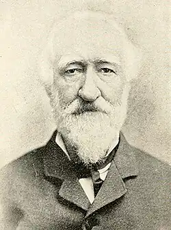 Man with a full white mustache and beard wearing a dark jacket and neck tie