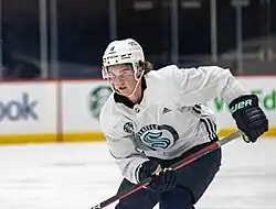Ice hockey player in a white Seattle Kraken skating with his stick in his hands