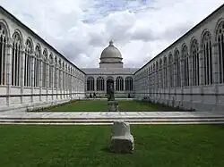 Vast cloister. Walls pierced with fine Gothic arcading, central lawn. Dome in the background