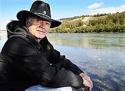 Carl Sidney, Chief Executive Officer of the Teslin Tlingit Council, seated beside a river.