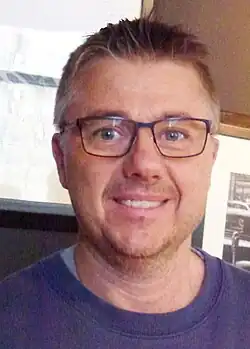 Headshot of Cambré in a purple shirt and glasses