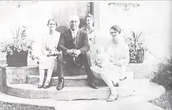 A man and three women seated on the front stoop of a house. One of the women is cradling a baby.
