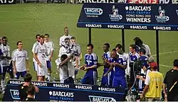 A coloured photograph of the Chelsea squad standing on a podium, celebrating their second Premier League Asia Trophy win.