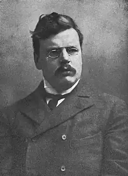 A moustachioed man with pince-nez glasses in a suit and a peacoat