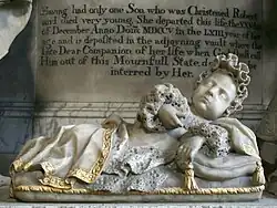 Reclining marble statue of a baby in lace clothing in front of a memorial slab