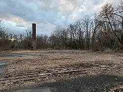 A once used chimney now stands alone next to a previously demolished building's cement foundation.
