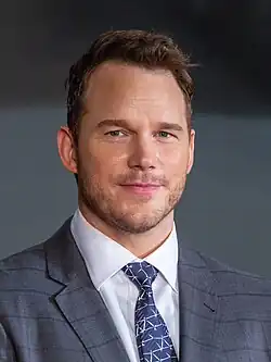 Head shot of Pratt smiling at the camera while wearing a suit and tie