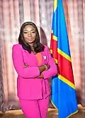 Congolese politician Christelle Vuanga wears a pink pantsuit near the flag of the Democratic Republic of the Congo in 2022