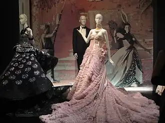 Elaborate evening gowns in various colors displayed on mannequins in a museum setting