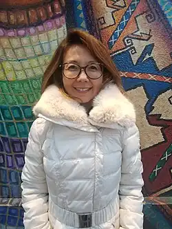 Ahn stands and smiles at the camera. She wears a fluffy winter parka and has glasses and shoulder-length reddish brown hair.