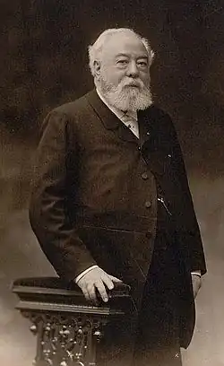 A man with white hair and beard standing in a suit