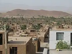 View looking out across Chupanan showing many adobe buildings and distant hills. Mostly tan spotted with dusty green trees.