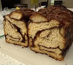 Cinnamon babka with streusel topping on cutting board, cut cross-wise to reveal streaks of cinnamon filling throughout.