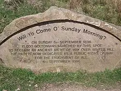 Stone with carved writing: "Will. Yo Come O' Sunday Morning? On Sunday 6th September 1896 10,000 Boltonians marched by this spot to reclaim an ancient right of way over Winter Hill. The path is now dedicated as a public right of way for the enjoyment of all. 6th September 1996"