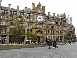 A partial view of the previous image but now a modern colour photograph; the building is a limestone facade and in the central tower there is a sign that says "CORN / EXCH / ANGE"